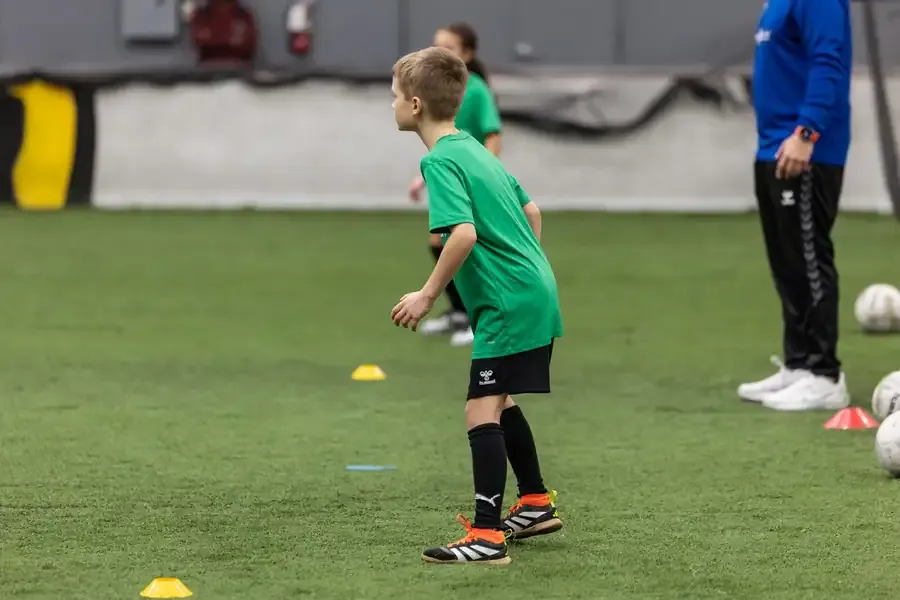 A young player dribbling through a drill on the indoor pitch