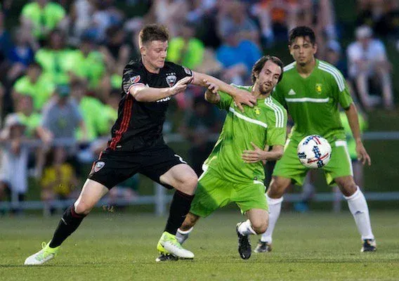 A player in a dark kit shielding the ball from two opponents in green during a match