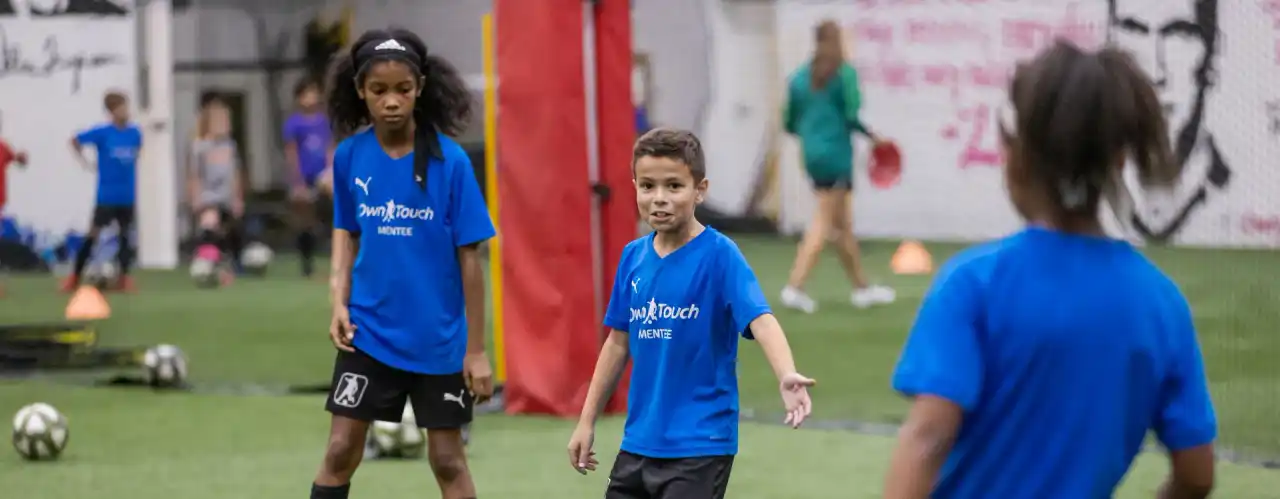 Mentees in blue Own Touch shirts during a ball-control drill on the indoor turf