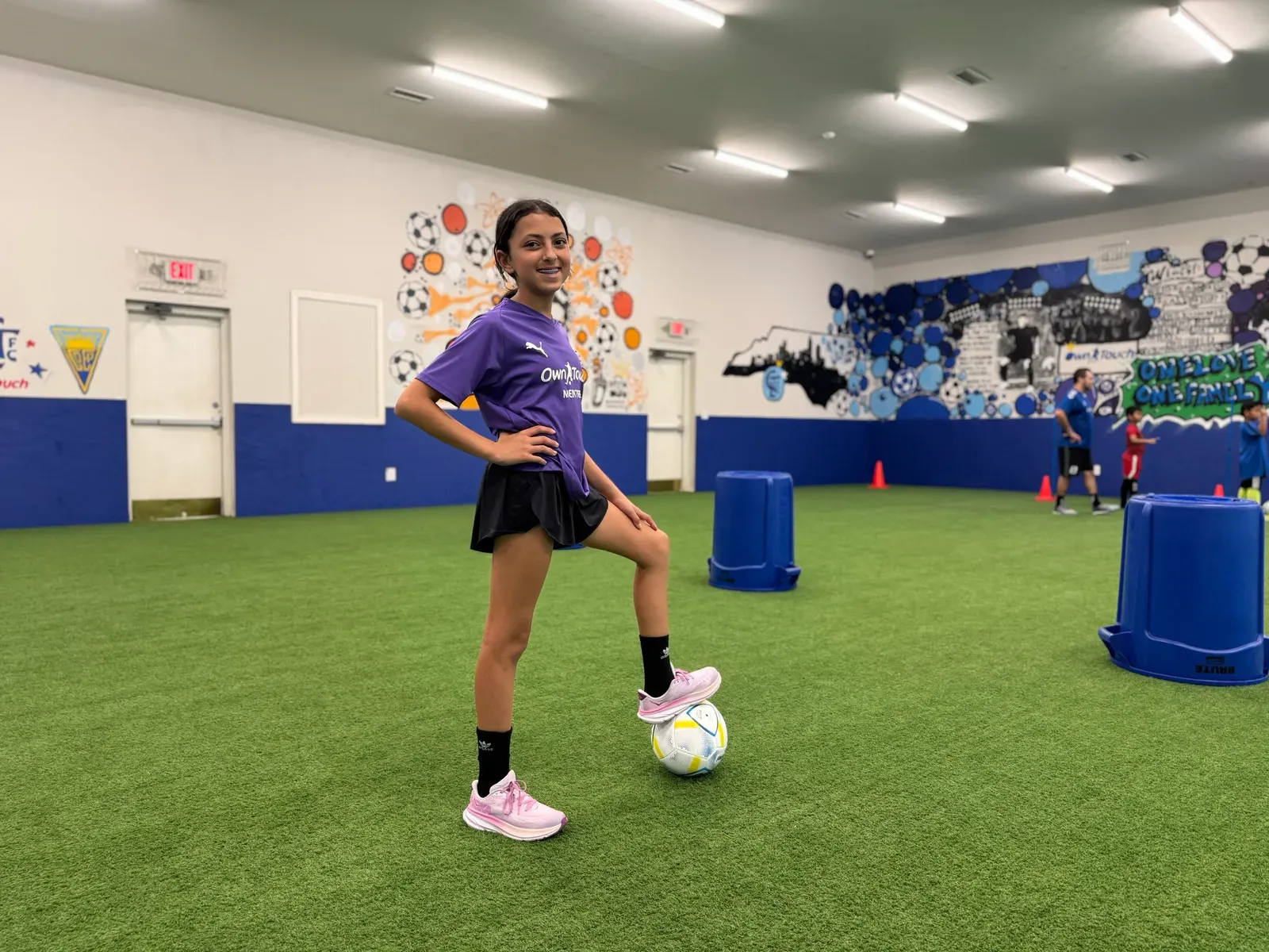 A player in a purple Own Touch shirt, foot on the ball, inside the Pineville studio