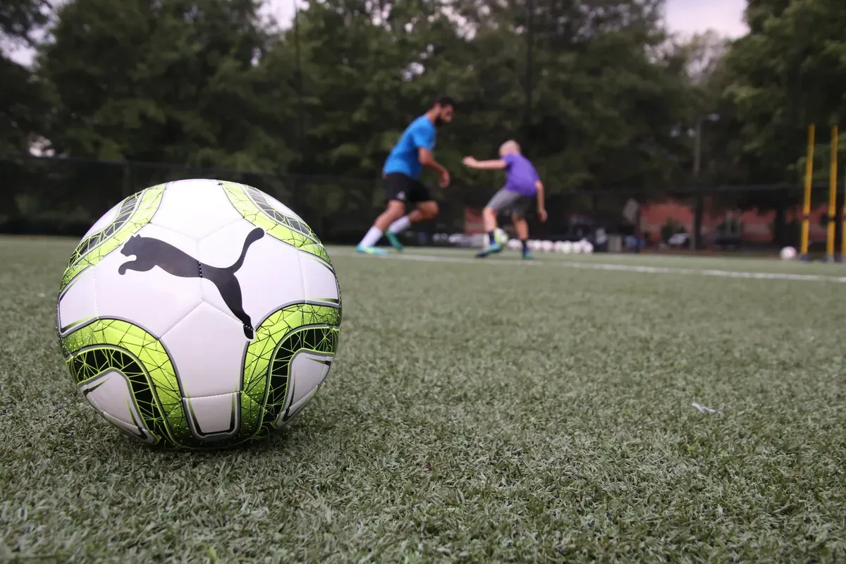 A match ball resting on the turf with two players training in the background