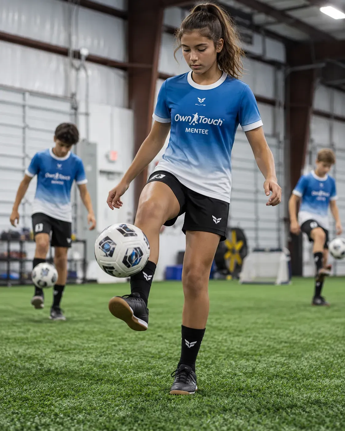 A Mentee in a blue Own Touch kit juggling the ball while teammates train behind