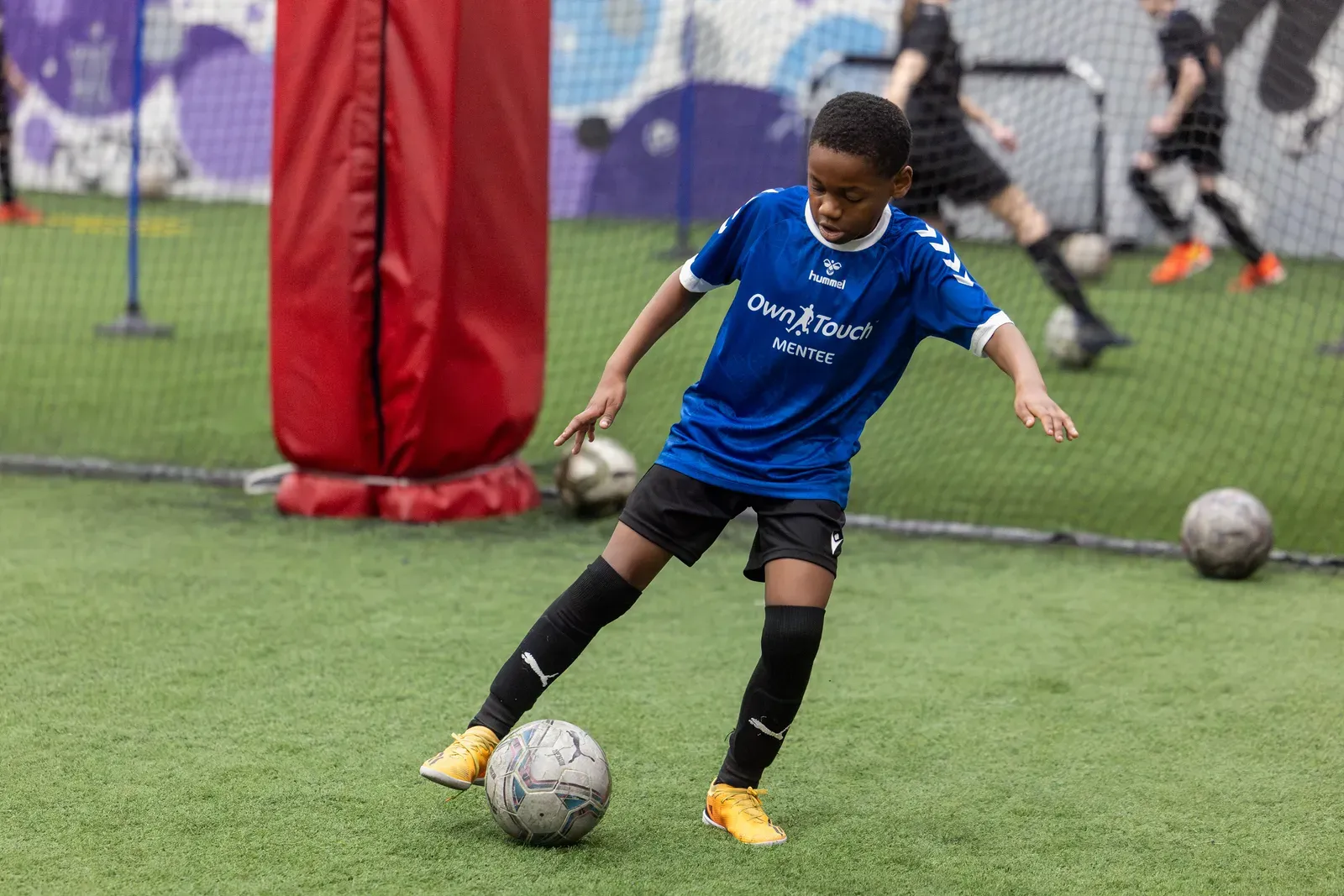 A Mentee in a blue Own Touch shirt working the ball beside a padded training post
