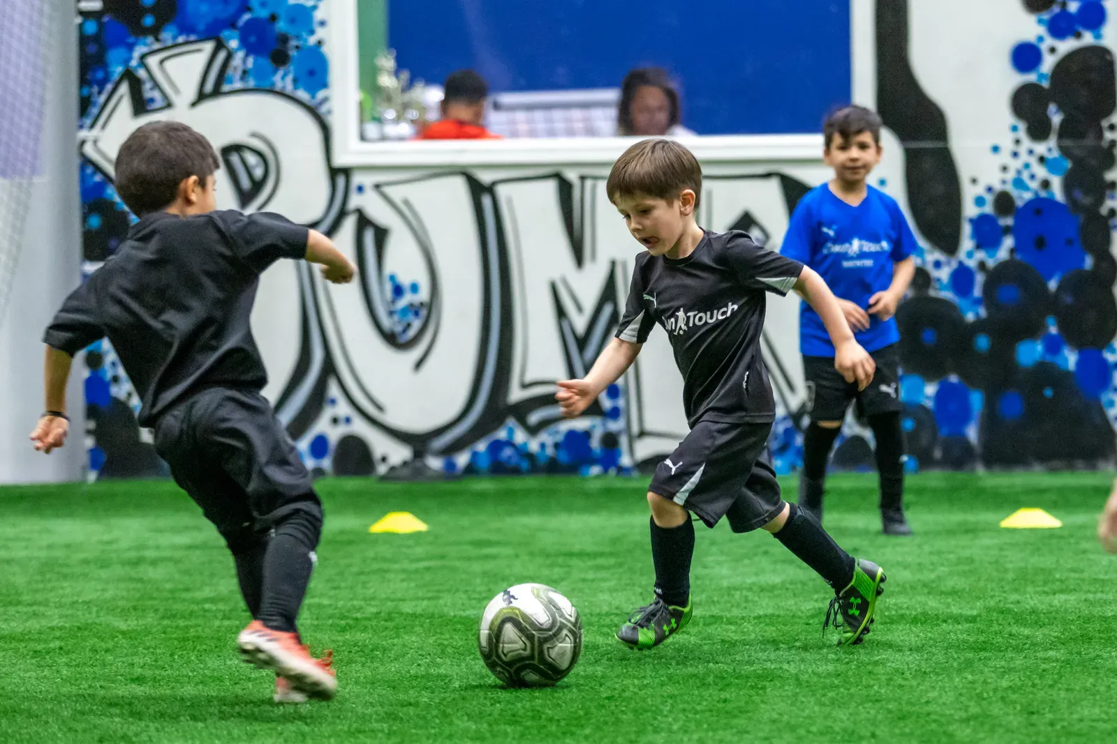 Mini Mentees in black Own Touch kits dribbling on the indoor pitch