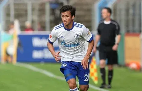 A young professional in a white Schalke kit driving forward with the ball