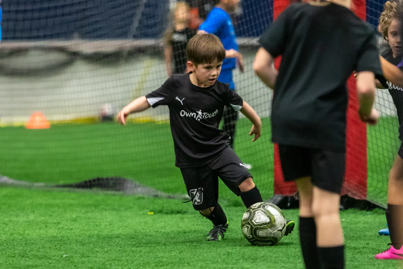 A Mini Mentee in a black Own Touch kit dribbling the ball