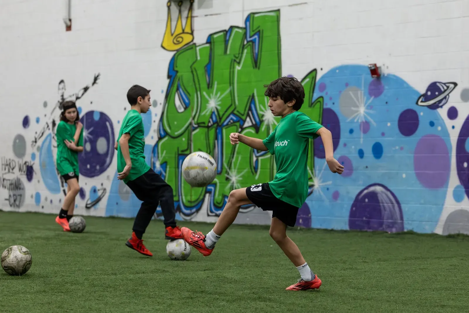 Prospects in green shirts striking and controlling balls in front of the Own Touch mural