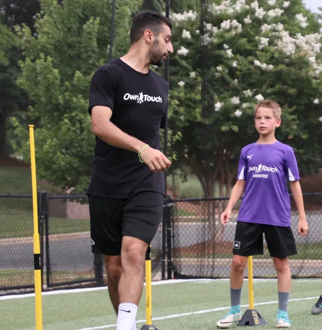 An Own Touch coach walking a young player in a Mentee shirt through a pole drill